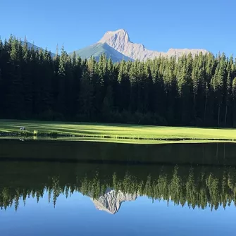 View of the Kananaskis golf course fairway with new sod surrounded by mountains, trees and water